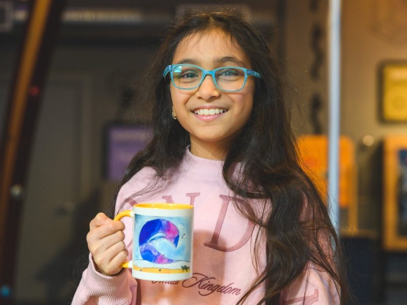 Doodles Academy past participant Swara Goyal holding a mug with her artwork that she was awarded.