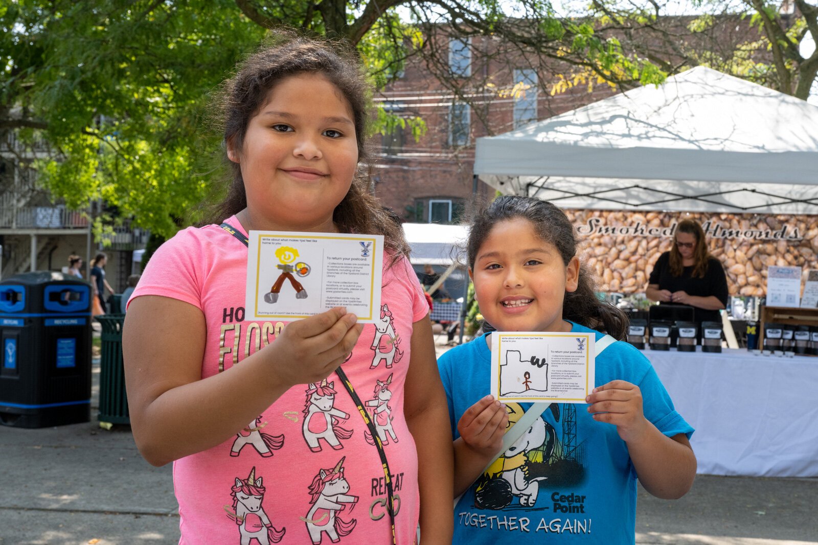 Young people hold up their love letters to Ypsilanti, created at an YpsiWrites booth at the Ypsilanti Depot Town Farmers Market.