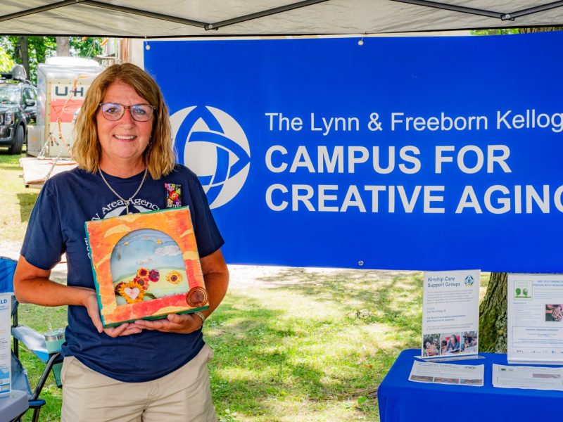 Amy Nichols, campus coordinator for the Region IV Area Agency on Aging, at the Campus for Creative Aging's booth in the South Haven Art Fair. She shows an example of the Window to Our World art project for care partners.