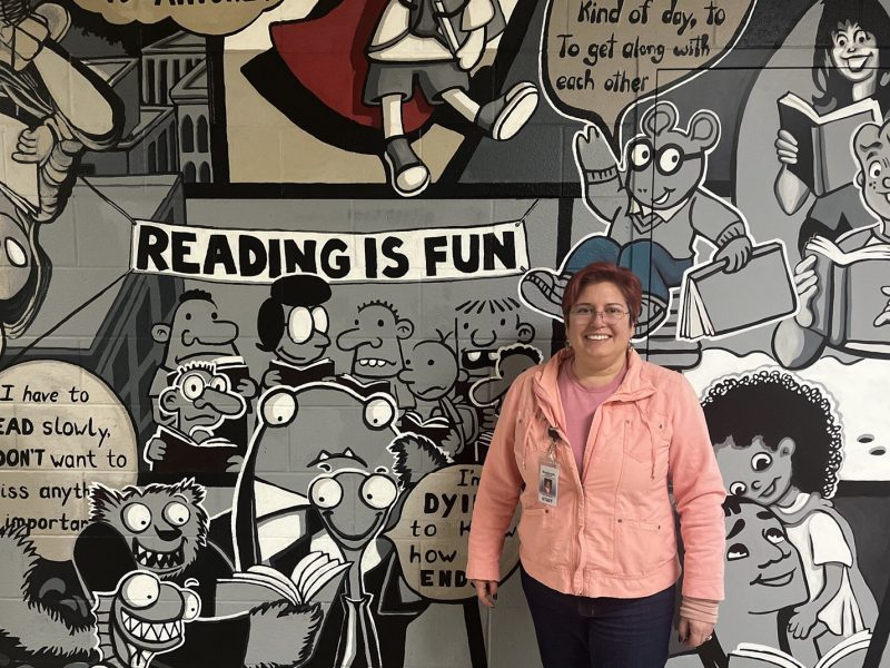 Stacy Schwartz stands in front of her mural, "Reading Can Take You Places," at Estabrook Elementary School.