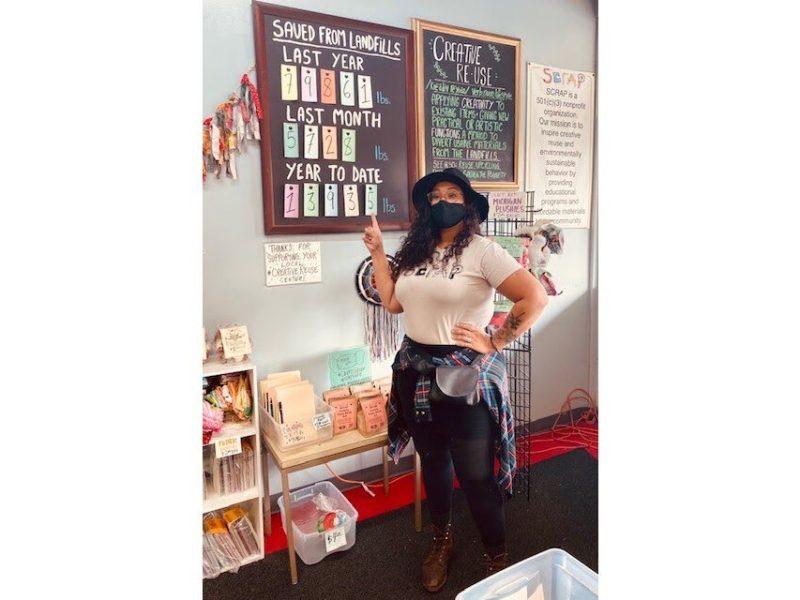 An employee at SCRAP Creative Reuse Ann Arbor points to a sign showing how much material the organization has diverted from landfills.