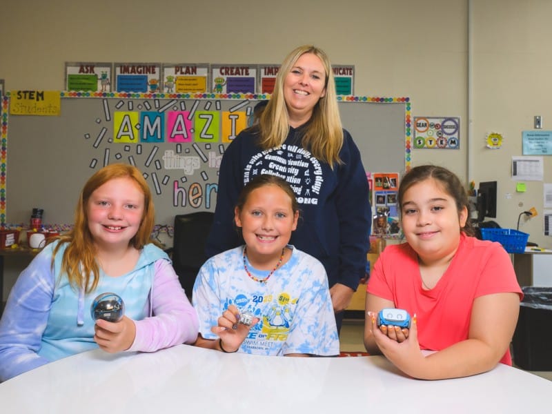 Brick Elementary students Grace Andrzejewski, Harper Lehto, and Victoria Giardini (front row) hold up robots that their teacher, Jodi VanHevel (in back), uses in class.