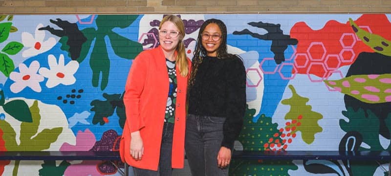 Artists Krista Skytta and Avery Williamson in front of their mural at Mitchell Elementary School in Ann Arbor.