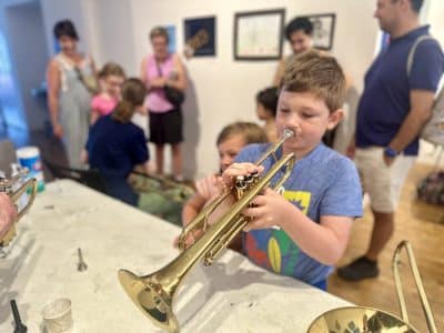 A young participant tries out a trumpet at an Ann Arbor Art Center PlayLab session that featured the Ann Arbor Symphony Orchestra's "Instrument Petting Zoo."
