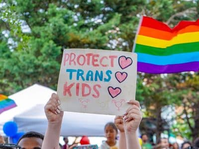 A protestor holds a sign reading "Protect Trans Kids."