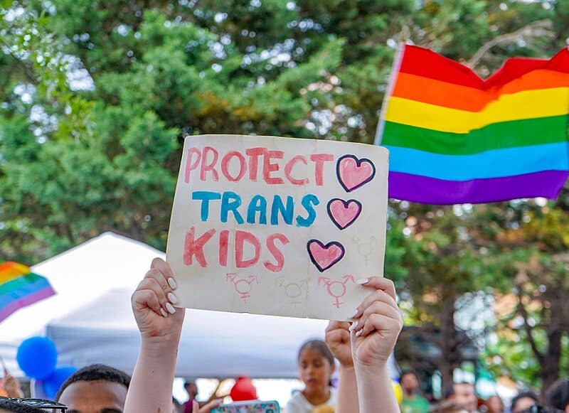 A protestor holds a sign reading "Protect Trans Kids."